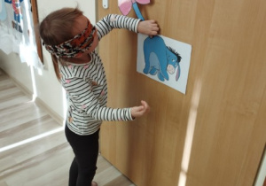 Dziewczynka z zawiązanymi oczami próbuje doczepić ogon Kłapouchemu