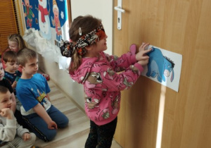 Dziewczynka z zasłoniętymi oczami doczepia ogon Kłapouchemu