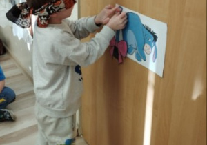 Chłopiec z zasłoniętymi oczami doczepia ogon Kłapouchemu