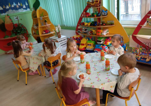 Chłopcy i dziewczynki siedzą przy dwóch stolikach. Jedzą pączki.