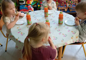 Dzieci siedzą przy stoliku i jedzą pączki.