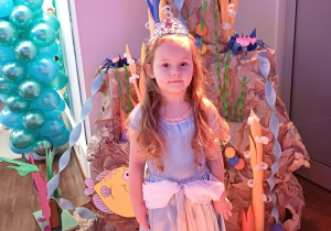 Dziewczynka prezentuje swoją suknię, pozując na tle kolorowej, podwodnej dekoracji
