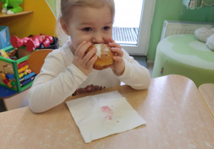 Dziewczynka w białej koszulce je pączka.