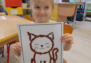 Dziewczynka w białej koszulce trzyma pracę kota.