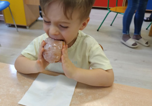 Chłopiec w żółtej koszulce zjada pączka.