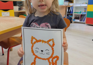 Dziewczynka w szarej koszulce trzyma pracę.