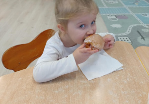 Dziewczynka w białej koszulce je pączka.