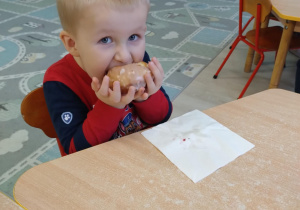 Chłopiec w czerwono - granatowej koszulce je pączka.