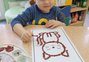 Chłopiec w granatowej koszulce siedzi przy stoliku z pracą z kotem.