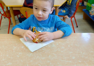 Chłopiec w niebieskiej koszulce je pączka.