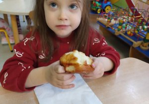 Dziewczynka w czerwonej koszulce je pączka.