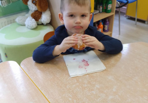 Chłopiec w granatowej koszulce je pączka przy stoliku.