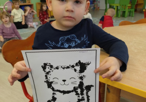 Chłopiec w granatowej koszulce trzyma wykonaną pracę kota.