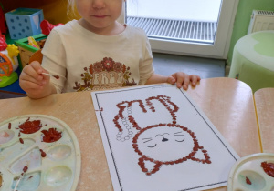 Dziewczynka w białej koszulce kropkuje patyczkiem kota.