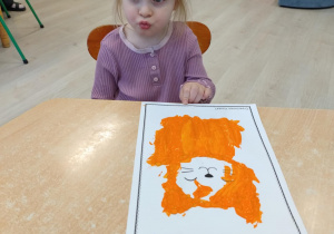 Dziewczynka w fioletowej koszulce siedzi przy stoliku w wykonanej pracy.