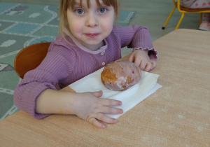 Dziewczynka w fioletowej koszulce je pączka.