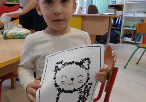 Chłopiec w białej koszulce trzyma pracę kota.