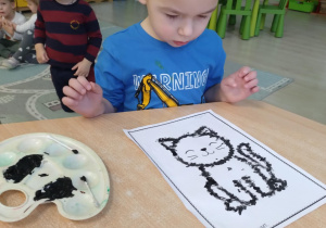 Chłopiec w niebieskiej koszulce kropkuje patyczkiem kontur kota.