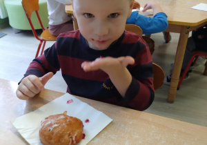 Chłopiec w czerwonej koszulce je pączka.