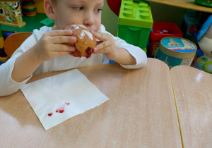 Chłopiec w białej koszulce je pączka.