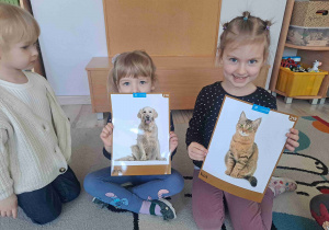 Dziewczunka trzyma grafikę psa, obok dziewczynka trzyma grafikę kota