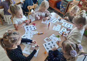 Dzieci siedzą przy stoliku wukonując kartę pracy