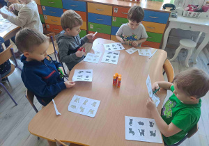 Dzieci siedzą przy stoliku wukonując kartę pracy