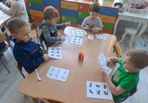 Dzieci siedzą przy stoliku wukonując kartę pracy
