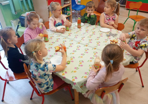 Dzieci jedzą pączki siedząc przy stole.