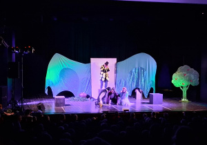 Scena z dekoracją do spektaklu Smocze opowieści. Aktorzy występują.