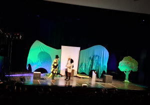 Scena z dekoracją do spektaklu Smocze opowieści. Aktorzy występują.