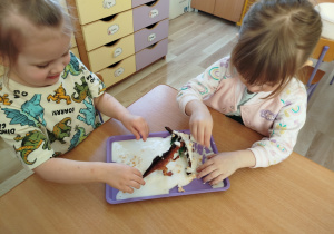 Dziewczynki bawią się cieczą nienewtonowską i figurkami dinozaurów