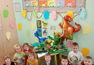 Dzieci z upominkami pozują do zdjęcia na tle wystawy plastycznej ,,Mój Dinozaur".