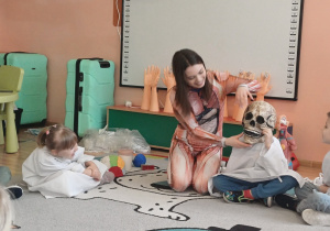 Dzieci uczestniczą w zajęciach edukacyjnych o budowie ciała, poznając części ciała podczas zabawy i obserwacji modeli