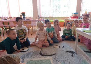 Dzieci siedzą z zainteresowaniem na dywanie