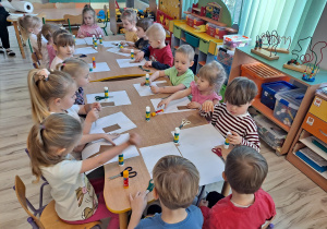 Dzieci przy stoliku wykonują pracę plastyczną