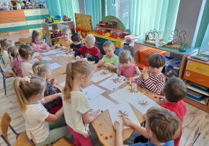 Dzieci przy stoliku wykonują pracę plastyczną