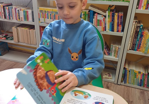 Chłopiec podczas wizyty w bibliotece ogląda książki