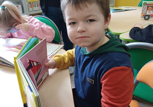 Chłopiec podczas wizyty w bibliotece ogląda książki