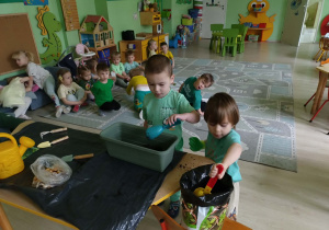 Chłopcy wsypują ziemię do doniczki