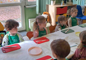 Dzieci siedzą przy stoliku, mają przygotowane talerzyki oraz noże do krojenia