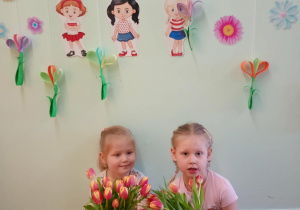 Dziewczynki pozują z kwiatami na tle dekoracji z okazji Dnia Kobiet.