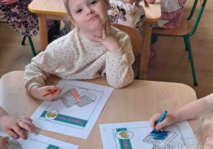 Dzieci przy stoliku wykonują karty pracy w tematyce Dnia Gofra