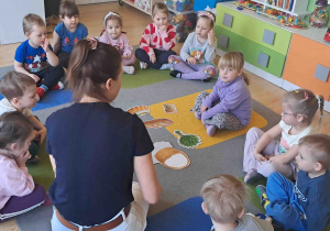 Dzieci oglądają rozłożone na dywanie ilustracje dotyczące koszyczka wielkanocnego