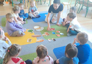 Dzieci oglądają rozłożone na dywanie ilustracje dotyczące koszyczka wielkanocnego