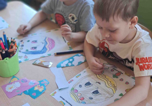 Dzieci przy stoliku ozdabiają kredkami i naklejkami wielkanocne pisanki