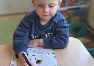 Dzieci przy stoliku ozdabiają kredkami i naklejkami wielkanocne pisanki