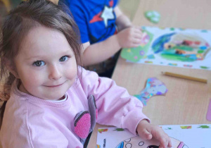 Dzieci przy stoliku ozdabiają kredkami i naklejkami wielkanocne pisanki