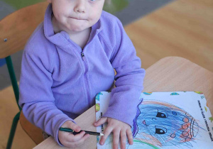 Dzieci przy stoliku ozdabiają kredkami i naklejkami wielkanocne pisanki