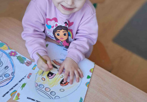 Dzieci przy stoliku ozdabiają kredkami i naklejkami wielkanocne pisanki